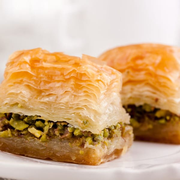 Two pieces of golden-brown baklava with pistachio filling on a white plate.