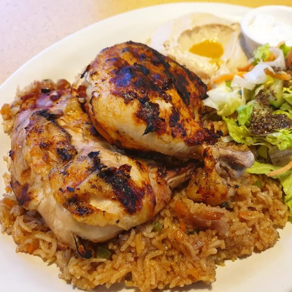 Grilled chicken pieces on a bed of rice, with hummus, salad, and white sauce.