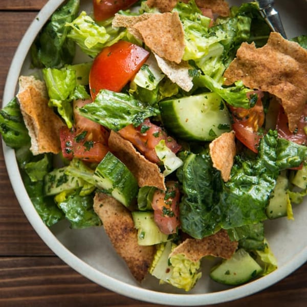 Close-up of a vibrant Fattoush salad with lettuce, tomatoes, cucumbers, and pita bread pieces.