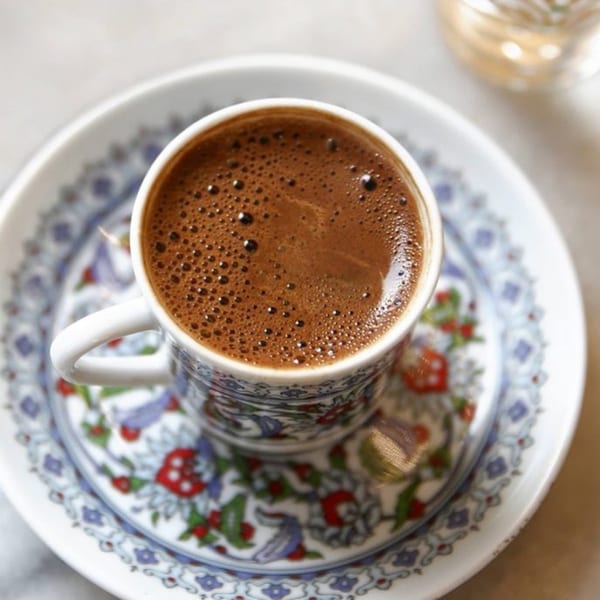 A foamy cup of Turkish coffee in a decorative cup and saucer from Sam's Pita and Kabab.