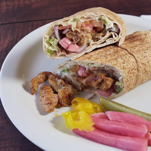 Two chicken shawarma wraps, one cut in half, with pickles and banana peppers on a white plate.